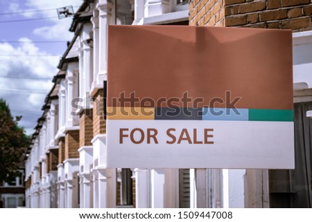 'FOR SALE' estate agency sign on street of houses