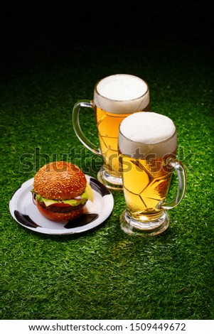 Two glasses of beer and hamburger on green grass.