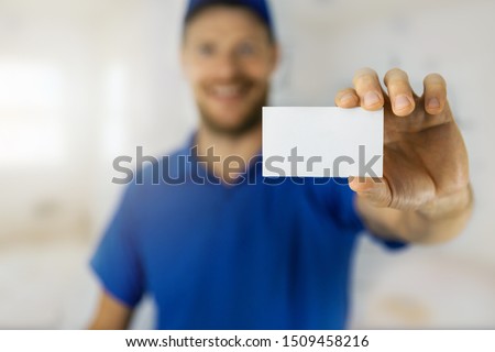 smiling handyman in blue uniform showing blank business card