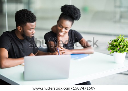Portrait of two colleagues working together at a cafe, discussing business ideas and plans, using laptop computer: African man holding a pen, pointing at the screen while presenting his project