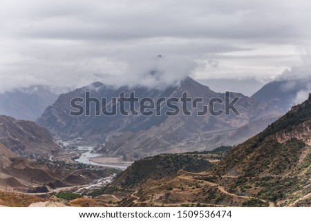 Image of mountains with green vegetation, smoke over tops, mountain river and houses at foot