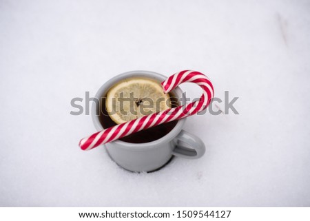 Tea mug with lemon and candy cane in the winter snow