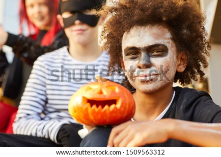 Portrait of African-American boy wearing Halloween costume looking at camera while sitting outdoors with friends, copy space