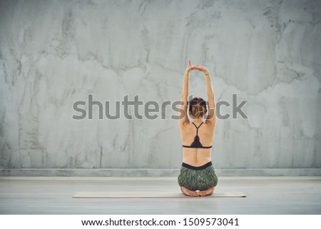 Woman sitting in on the mat in Side Mountain Pose. Backs turned.