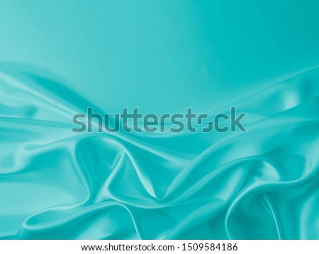 Smooth elegant wavy turquoise silk or satin luxury cloth fabric texture, abstract background design.