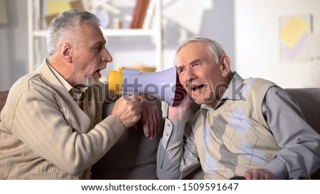 Senior man shouting bullhorn to deaf friend, old aged health, deafness treatment Royalty-Free Stock Photo #1509591647
