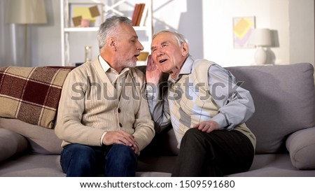 Old man talking to deaf friend sitting on sofa at home, hearing disease, problem Royalty-Free Stock Photo #1509591680