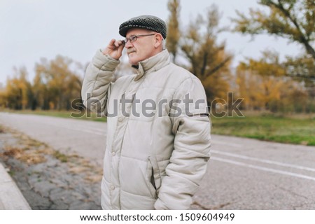 An old man in a jacket and a cap holds glasses in his hand and looks into the distance. The concept of retirement age and poor vision. Hyperopia, myopia. Royalty-Free Stock Photo #1509604949
