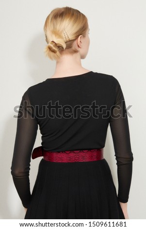Cropped back view shot of a blond girl, posing on a white background. She is wearing black gown with transparent sleeves and crimson snake print wide belt. Her hair pulled back with bobby pins. 