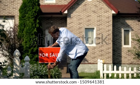 House owner installing for sale signboard in front of luxury building, moving