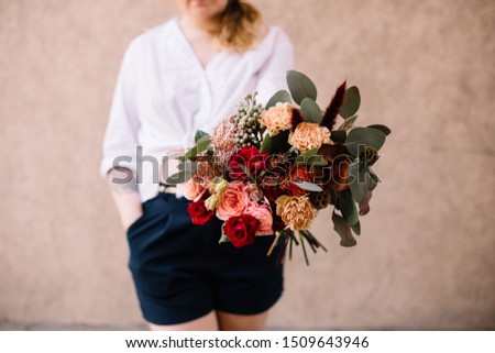 Very nice young woman holding big and beautiful bouquet of fresh roses, carnations, nutan, eucalyptus, brunia in red and pink colors, cropped photo, bouquet close up on the wooden background