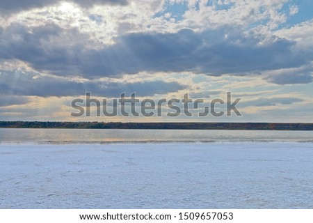 The photo was taken in Ukraine, in Odessa region. In the picture, the shore of a salty estuary covered with a crust of salt, like snow. A picturesque cloudy sky is visible above the estuary.
