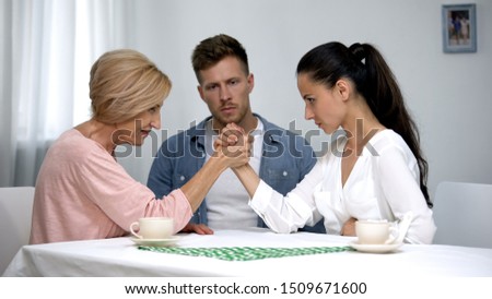 Man looking at mother and wife during arm wrestling competition, family fight