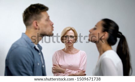 Displeased mother with hands crossed looking at young couple preparing to kiss