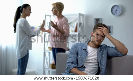 Exhausted male listening wife and mother-in-law arguing at home, rivalry Royalty-Free Stock Photo #1509671828