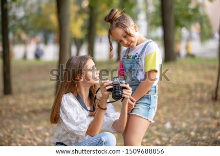 Two girls on the street make a video for the Internet, record a video blog for the camera. Children with photo appart in a city park