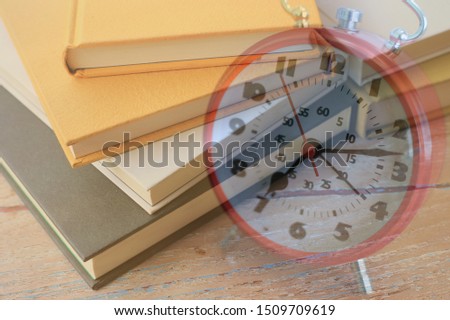 A stacked picture of many books on a red alarm clock