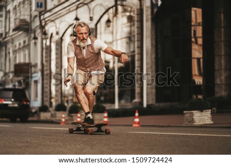 Portrait of handsome man in white shirt on sunset evening in summer. Stylish guy ride on skateboard on city street. Urban male lifestyle on buildings background Royalty-Free Stock Photo #1509724424