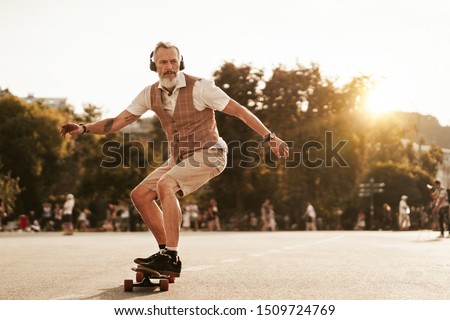 Skater posing in sunset evening on city street. Stylish hipster man with longboard ride near road on buildings background. Portrait of sport male model in urban style. Traveler. Tourist Royalty-Free Stock Photo #1509724769