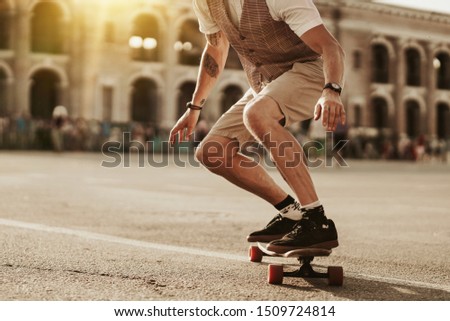 Urban man lifestyle. Stylish man ride on skateboard in white shirt on city street. Portrait of handsome bearded hipster male near road on buildings background. Royalty-Free Stock Photo #1509724814