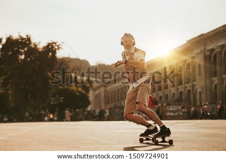 Portrait of handsome man in white shirt on sunset evening in summer. Stylish guy ride on skateboard on city street. Urban male lifestyle on buildings background Royalty-Free Stock Photo #1509724901