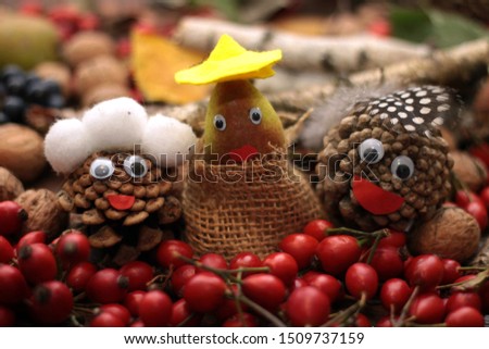 Three faces made of cones with eyes and mouth, head cover surounded by falll items as rose hip, nuts, grapes, leaves. Autumn background.