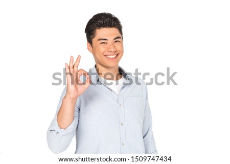 happy asian man showing okay sign while smiling at camera isolated on white