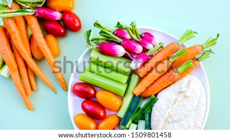 Fresh Vegetable Crudite Platter With Hummus and Baby Carrots, Radishes, Cucumber, Celery and Tomatoes, On A Green Background