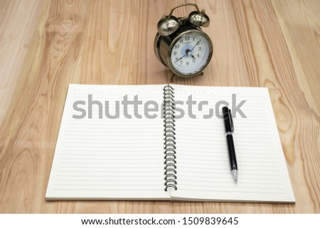 Blank notebook with pen and clock on the wooden table business concept.
