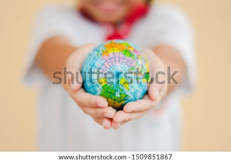 A girl is holding the globe by her hands with yellow background. The concept of saving the world and caring for the world.
