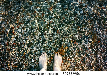Beautiful female legs on small stones in the sea 