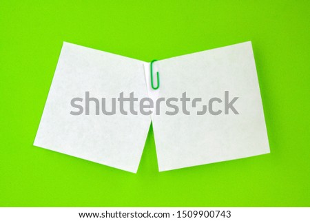 Two white leaflets for notes stapled with a paper clip on a green background. Copy space.