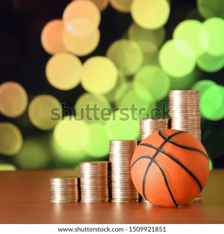 Basketball and stacks of golden coins in growth graph on the blurred bokeh background