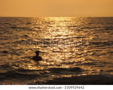 Man swimming and looking towards a sailboat in Santa Monica beach during the sunset. California USA