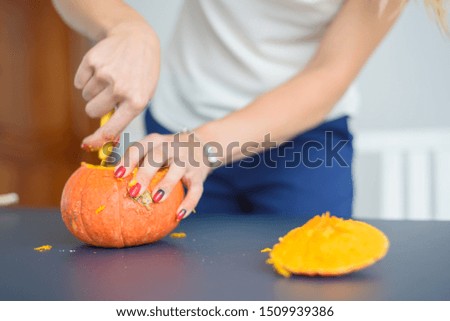 A woman carves her face on a pumpkin for a Halloween lamp on a black table. Close-up female hands making Jack-o'-lantern to the eve of all saints.
