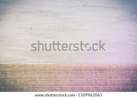 Knitted beige soft fabric on a light painted wooden board. Background, blank for design. Original tinted color photo in purple tones. Horizontal picture