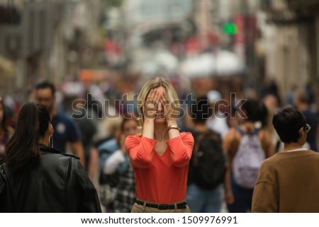 Sad depressed woman covers his eyes with his hands surrounded by people walking in crowded street. Panic attack in public place.  Royalty-Free Stock Photo #1509976991