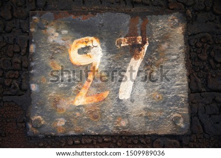 Number twenty-seven, 27, painted on an old rusty plate.