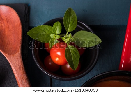 Tomette Sauce in Red Pan with Black Background on Top of Black and Green Oil Wood with Wooden Spoon, Cherry Tomato on Black Slate and Marigold Leaves