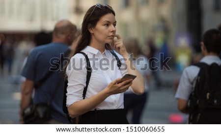 Girl on the street among the crowd of passers-by, photos in the style of surveillance. young woman in the city uses her phone to find a route, uses the Internet and mobile applications.
