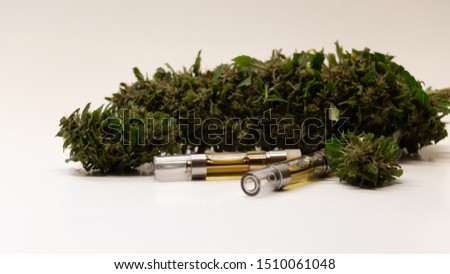 Hemp derived CBD oil infused vape smoking refill cartridges on white background with large hemp flower buds. Generic product image. Popular cigarette smoking substitute. Shallow focus.