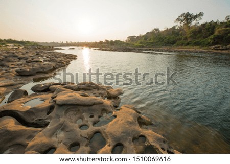 Rocks with many holes by the river and sunset