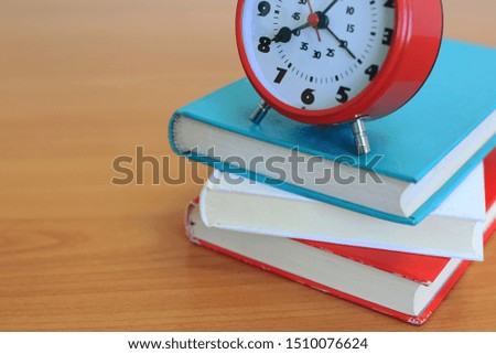 Close-up of several colored books stacked on a wooden table Red antique alarm clock placed on top selective focus and shallow depth of field