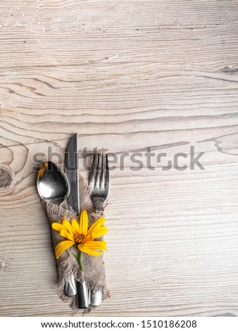 Rustic table setting with linen napkin, cutlery, yellow lower on wooden table. Holiday table decoration. Romantic dinner. Copy space