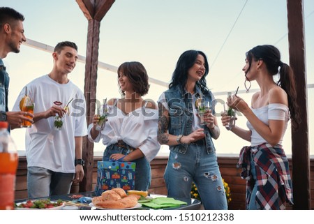 It's my birthday. Cheerful young people chatting and drinking cocktails at a rooftop party
