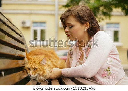big red maine coon cat is scary and sad. young owner woman hugs and strokes her orange pet in stress from first walk outdoor.