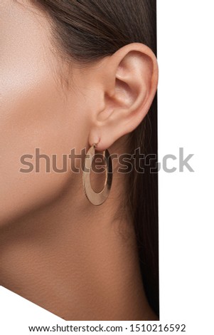 Closeup side view shot of woman with bronze skin and straight dark hair wearing golden metallic congo earring made in the shape of wide flat ring. 