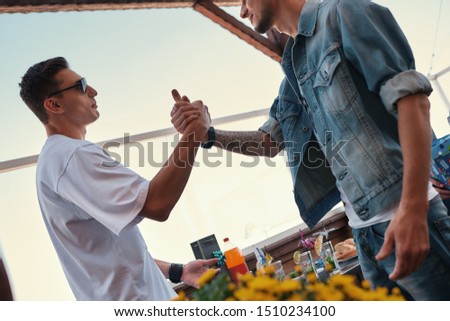 My best friend. Two young and handsome men shaking hands while standing on the roof and enjoying party