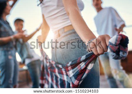 Carefree time. Close up photo of a woman in casual clothes holding checkered shirt behind back while standing on rooftop terrace with her friends