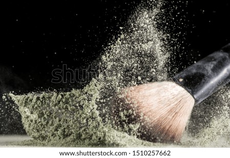 cosmetic brush falls into powder and sprays it on a black background